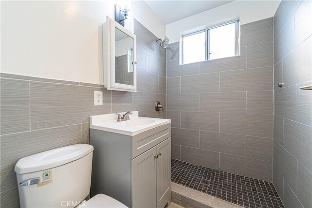 bathroom featuring toilet, a tile shower, vanity, and tile walls