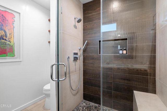 full bathroom with tile patterned flooring, baseboards, a tile shower, and toilet