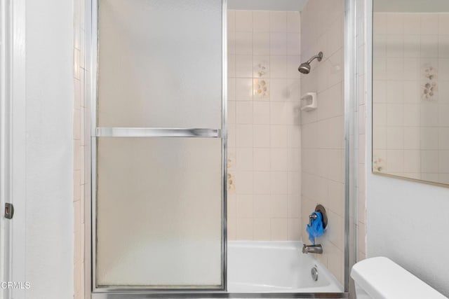 bathroom featuring combined bath / shower with glass door and toilet