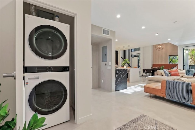 clothes washing area with stacked washing maching and dryer and a notable chandelier