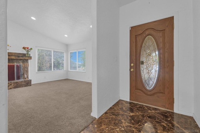 carpeted entrance foyer with lofted ceiling and a stone fireplace