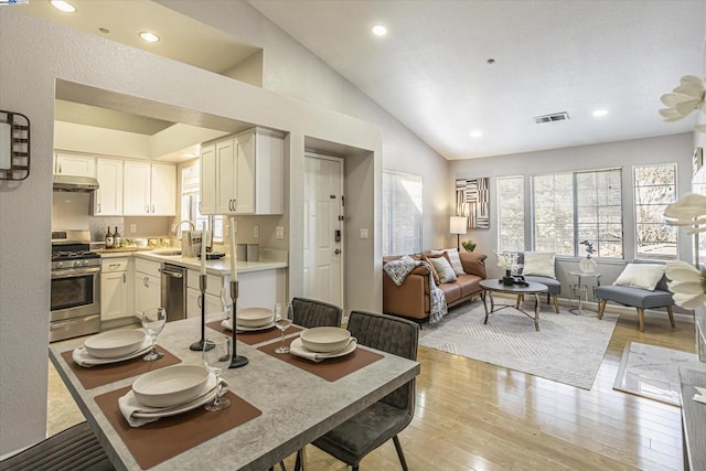 dining space featuring high vaulted ceiling, sink, and light hardwood / wood-style floors