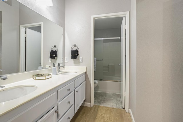 full bathroom featuring wood-type flooring, combined bath / shower with glass door, vanity, and toilet