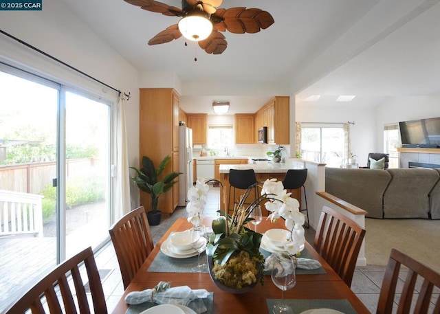 dining space with ceiling fan, a fireplace, and light tile patterned flooring