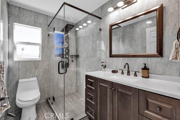 bathroom with toilet, tile walls, a shower with shower door, and vanity