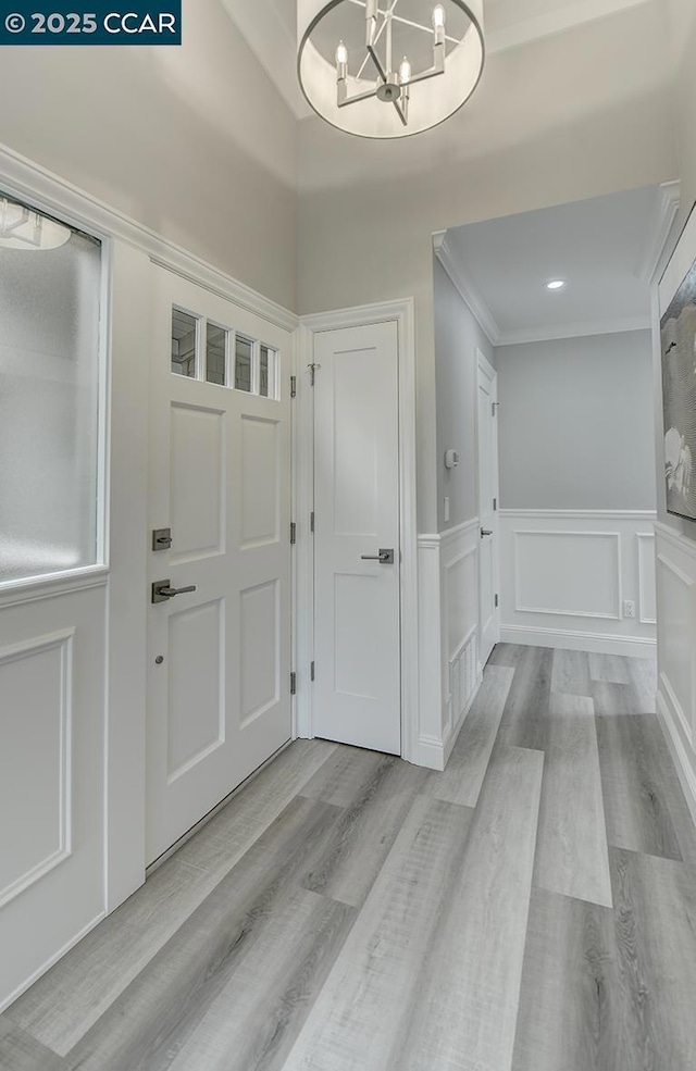 entryway featuring an inviting chandelier, ornamental molding, and light hardwood / wood-style flooring