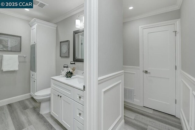 bathroom with toilet, vanity, crown molding, and hardwood / wood-style flooring