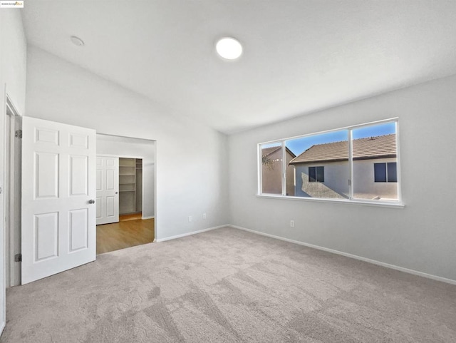 unfurnished bedroom featuring a spacious closet, a closet, vaulted ceiling, and carpet floors