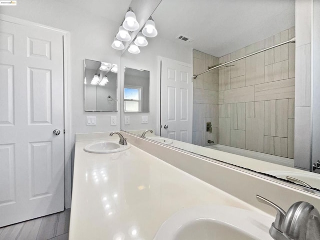 bathroom featuring hardwood / wood-style flooring, vanity, tiled shower / bath, and an inviting chandelier