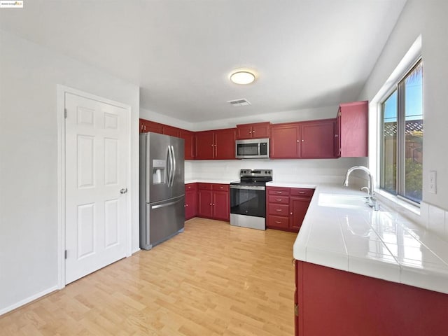 kitchen with appliances with stainless steel finishes, sink, and light hardwood / wood-style floors