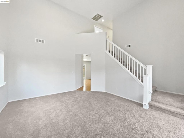 unfurnished living room featuring carpet flooring and a high ceiling