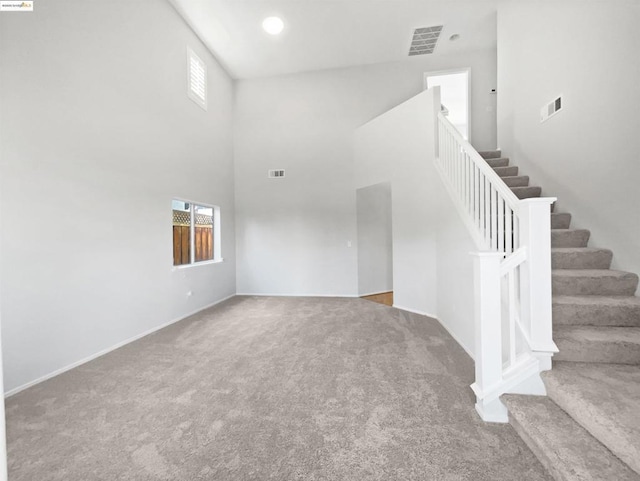 unfurnished living room featuring carpet floors and a towering ceiling