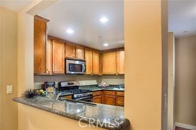 kitchen with kitchen peninsula, dark stone counters, and stainless steel appliances