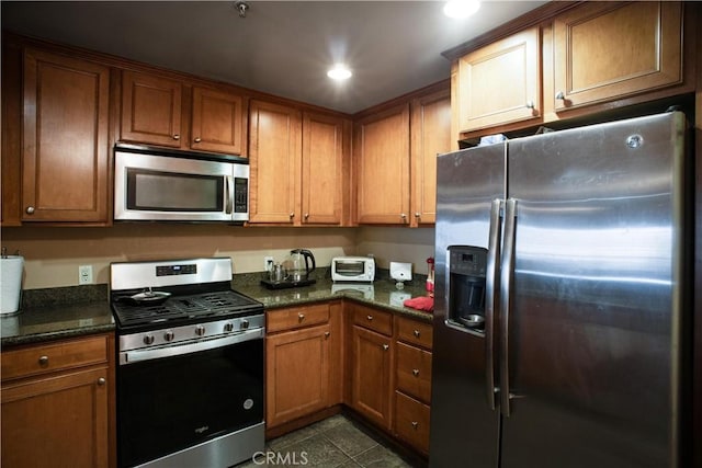 kitchen with dark tile patterned floors, appliances with stainless steel finishes, and dark stone counters