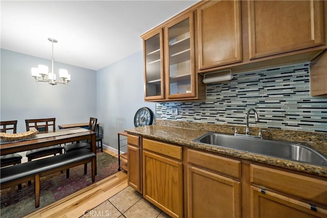 kitchen with tasteful backsplash, dark stone countertops, sink, an inviting chandelier, and hanging light fixtures