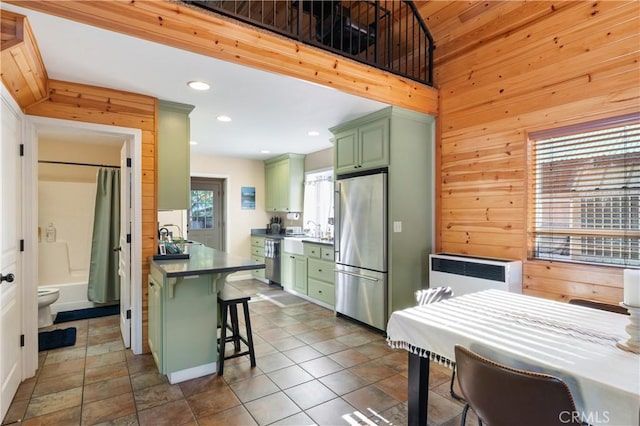 kitchen featuring appliances with stainless steel finishes, radiator, wooden walls, green cabinets, and a breakfast bar area