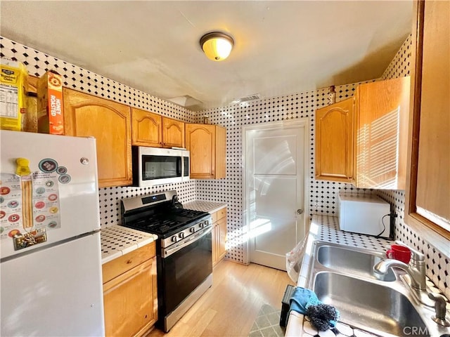 kitchen with backsplash, sink, stainless steel appliances, and light hardwood / wood-style flooring