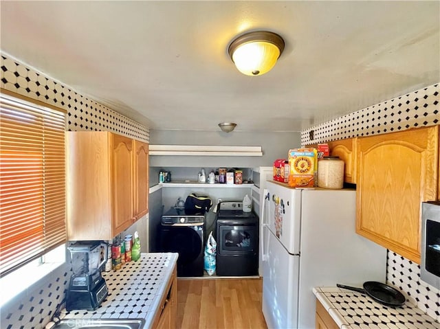 kitchen featuring white fridge, washing machine and clothes dryer, light hardwood / wood-style flooring, light brown cabinets, and tile counters