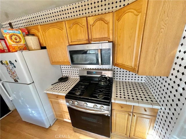 kitchen with tasteful backsplash, appliances with stainless steel finishes, tile countertops, and light hardwood / wood-style floors