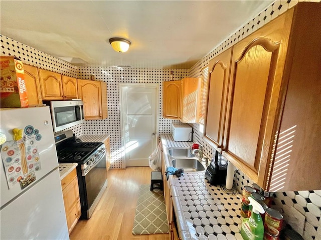 kitchen with appliances with stainless steel finishes, sink, and light hardwood / wood-style flooring