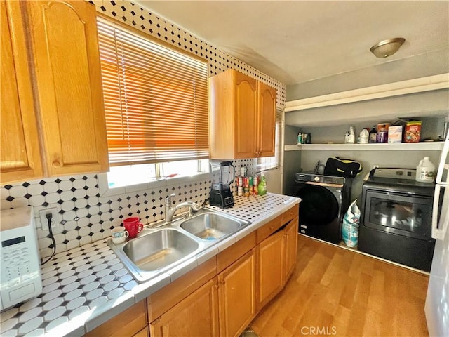 kitchen featuring washer and clothes dryer, light hardwood / wood-style floors, sink, decorative backsplash, and tile countertops