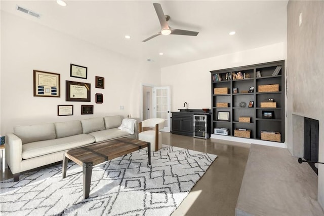 living room featuring beverage cooler, a premium fireplace, sink, ceiling fan, and concrete flooring