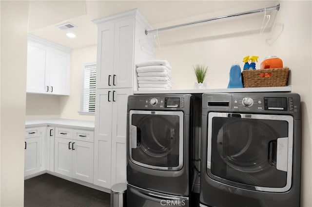 laundry room with dark tile patterned floors, washing machine and dryer, and cabinets