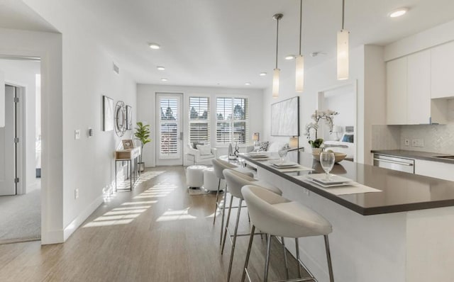 kitchen featuring tasteful backsplash, light hardwood / wood-style floors, white cabinets, a kitchen bar, and decorative light fixtures