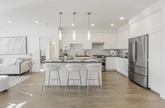 kitchen with decorative light fixtures, tasteful backsplash, white cabinets, a kitchen breakfast bar, and stainless steel appliances