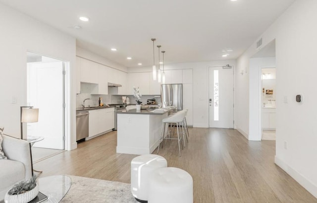 kitchen with white cabinetry, decorative light fixtures, light hardwood / wood-style flooring, and stainless steel appliances