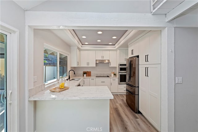 kitchen with white cabinets, kitchen peninsula, fridge, a tray ceiling, and black electric cooktop