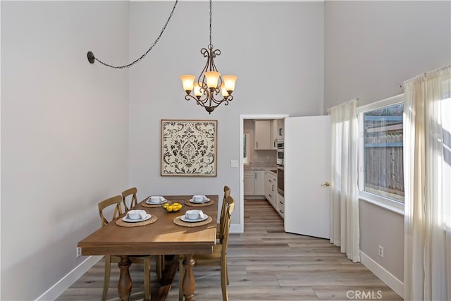 dining room featuring a towering ceiling, a chandelier, and light hardwood / wood-style floors