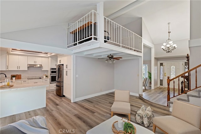 living room featuring ceiling fan with notable chandelier, a high ceiling, sink, and light wood-type flooring