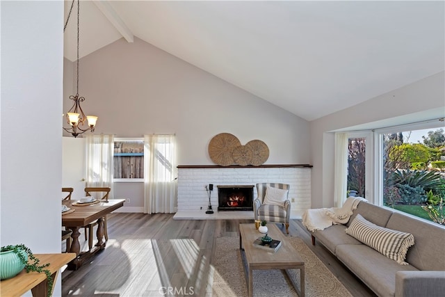 living room with a brick fireplace, hardwood / wood-style floors, an inviting chandelier, and vaulted ceiling with beams