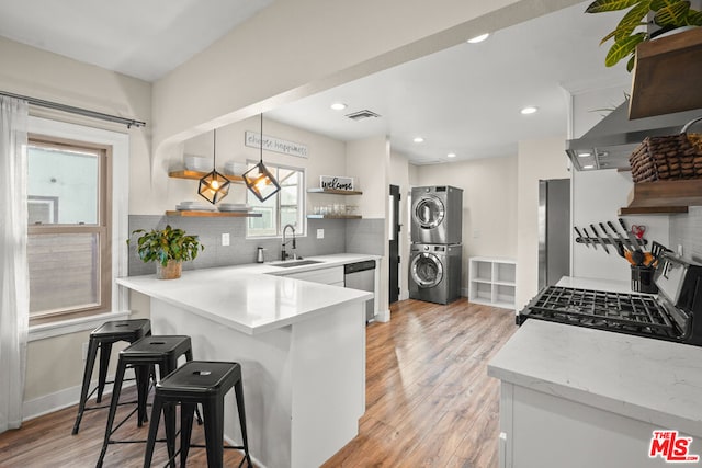 kitchen featuring white cabinetry, stainless steel dishwasher, a kitchen breakfast bar, kitchen peninsula, and stacked washer / dryer