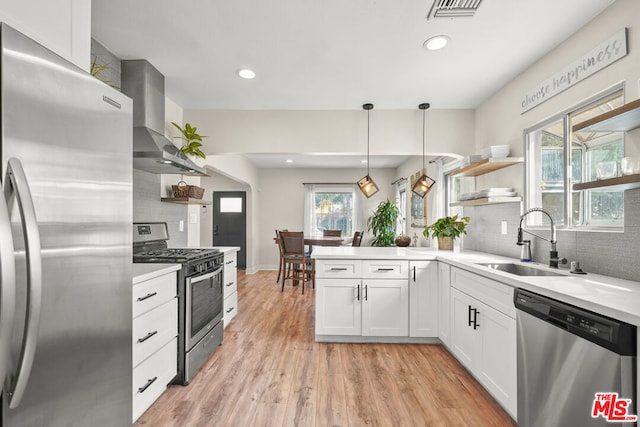 kitchen with pendant lighting, sink, white cabinets, stainless steel appliances, and wall chimney range hood