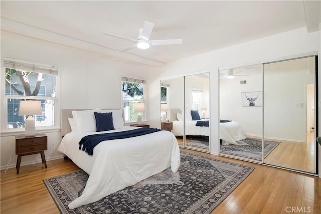 bedroom with ceiling fan, hardwood / wood-style flooring, and two closets