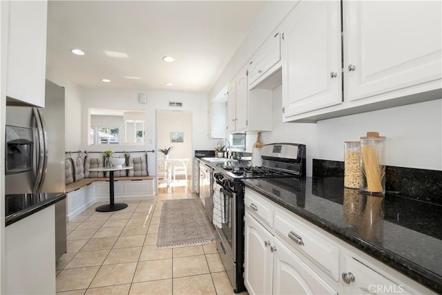 kitchen with white cabinetry, stainless steel appliances, light tile patterned flooring, dark stone counters, and sink