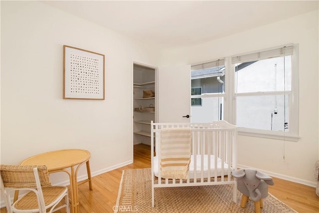 bedroom featuring wood-type flooring, a nursery area, and a walk in closet