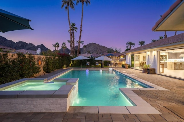 pool at dusk featuring an in ground hot tub, a patio area, pool water feature, and a mountain view