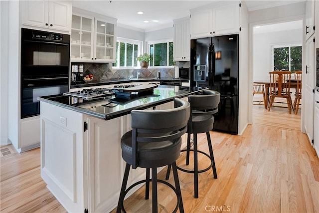 kitchen with white cabinets, black appliances, a kitchen island, backsplash, and light wood-type flooring