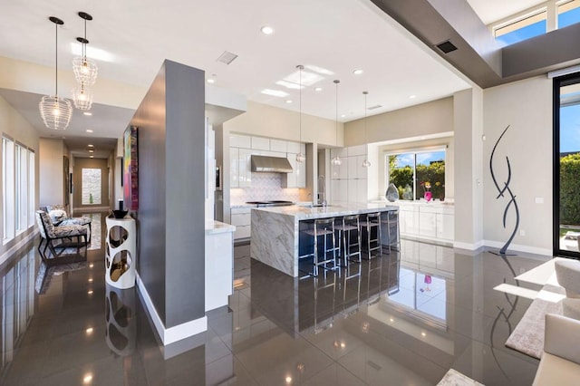 kitchen with tasteful backsplash, decorative light fixtures, ventilation hood, dark tile patterned floors, and a large island