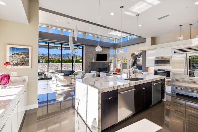 kitchen featuring appliances with stainless steel finishes, decorative light fixtures, white cabinetry, a kitchen island with sink, and light stone countertops