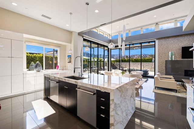 kitchen with sink, light stone counters, decorative light fixtures, dark tile patterned floors, and a kitchen island with sink