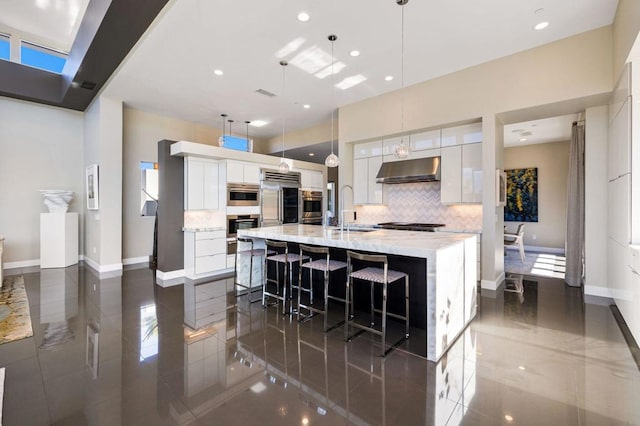 kitchen featuring a spacious island, a kitchen bar, built in refrigerator, decorative light fixtures, and white cabinets