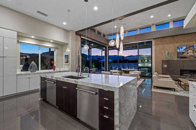 kitchen with pendant lighting, sink, a kitchen island with sink, light stone counters, and dark brown cabinets