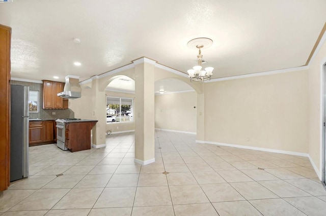 kitchen featuring decorative light fixtures, island exhaust hood, ornamental molding, stainless steel refrigerator, and gas range