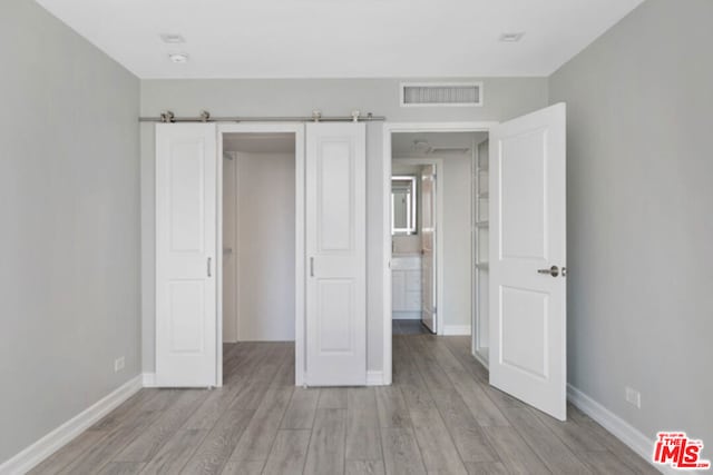 unfurnished bedroom featuring light hardwood / wood-style floors and a barn door