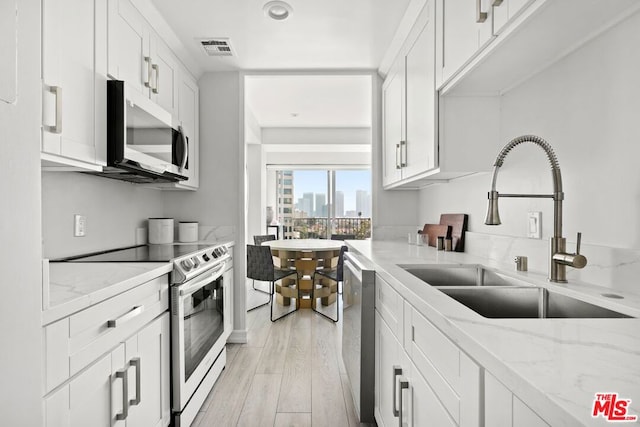 kitchen featuring stainless steel appliances, white cabinets, light stone counters, and sink