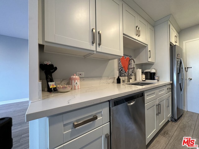 kitchen featuring sink, white cabinetry, light wood-type flooring, appliances with stainless steel finishes, and light stone counters